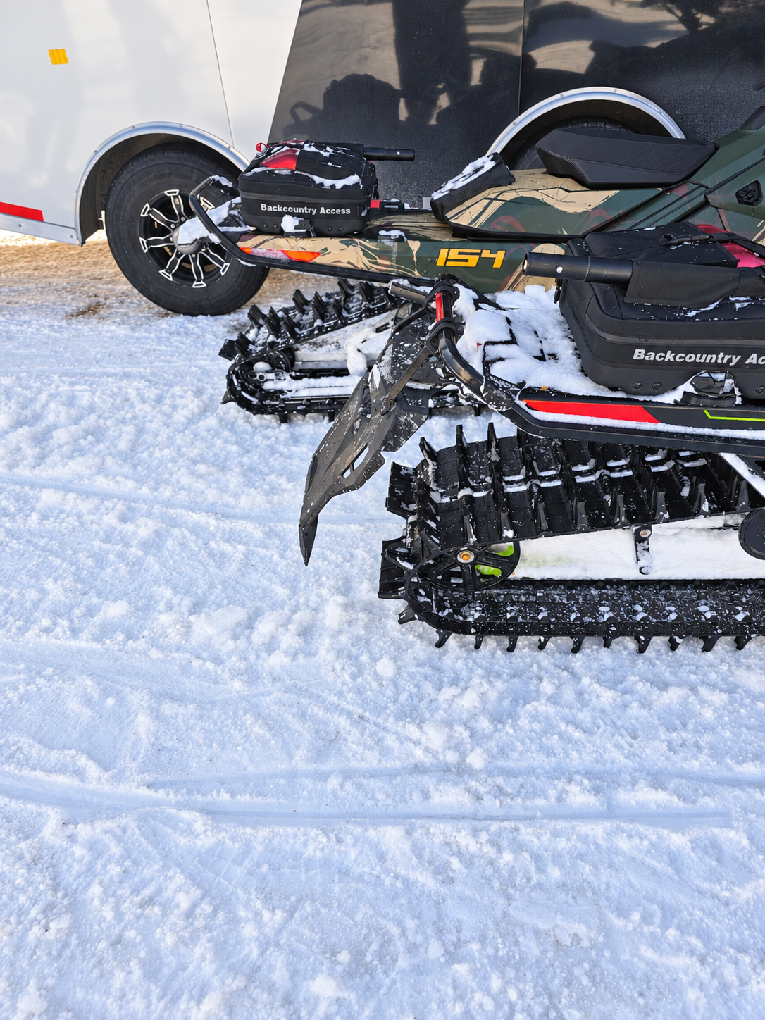 Side view of the snowflap behind the track beside another snowmobile and a trailer