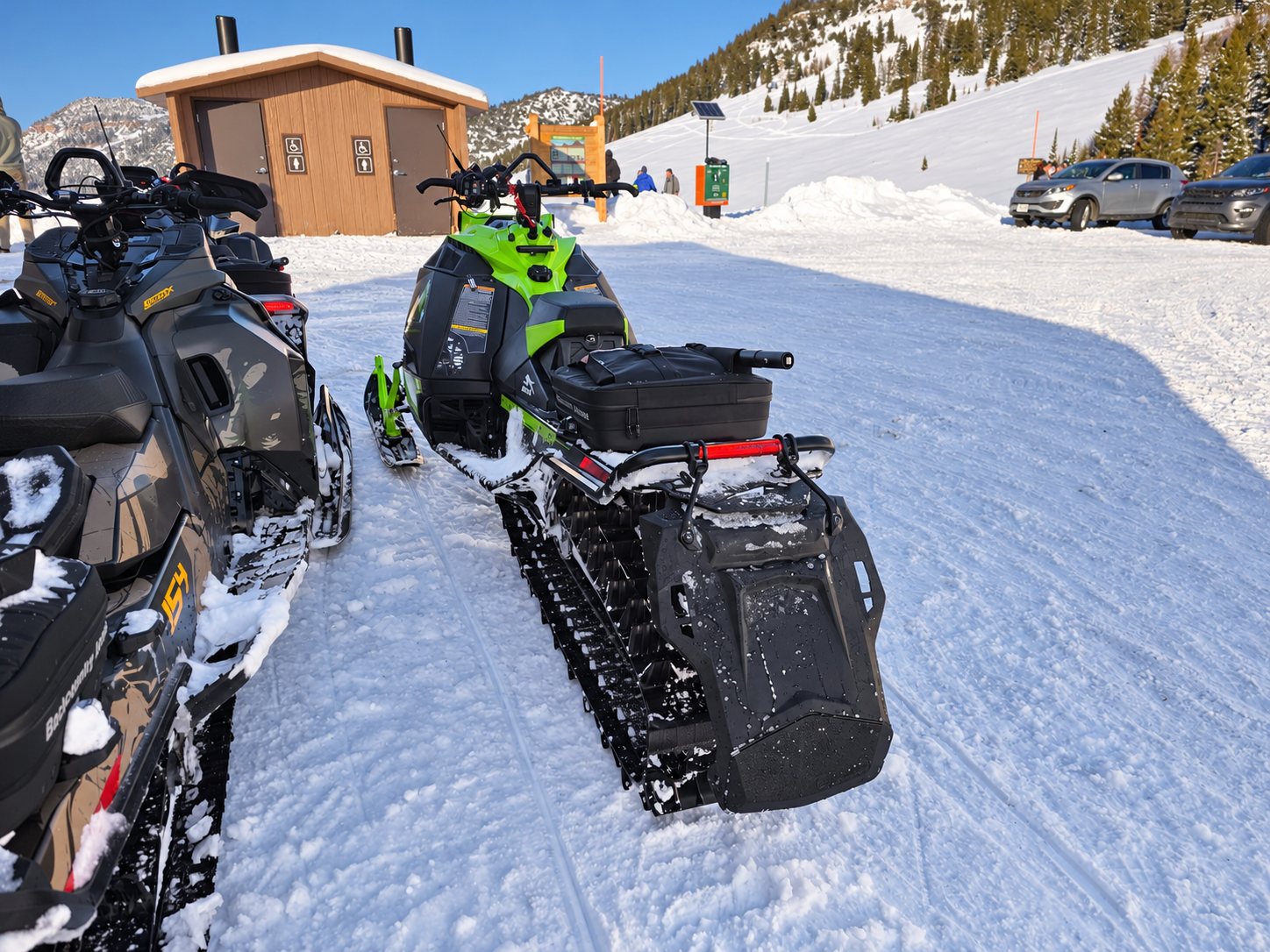 Green Catalyst with the development snowflap setup parked with other sleds at a snowy trailhead